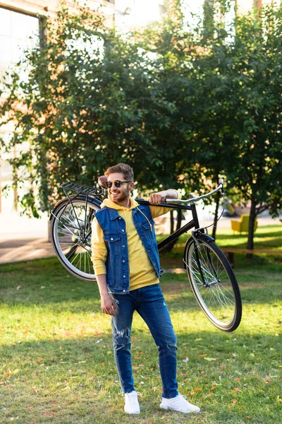 Jovem homem alegre em óculos de sol com bicicleta retro no parque — Fotografia de Stock