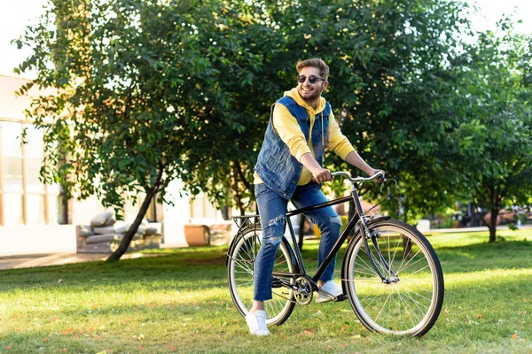 Молодий усміхнений чоловік в сонцезахисних окулярах верхи ретро велосипед в парку — стокове фото