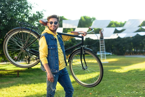 Jovem sorridente homem em óculos de sol com bicicleta retro no parque — Stock Photo