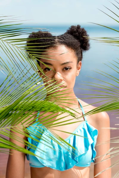 Portrait of serious african american woman near palm leaves in front of sea — Stock Photo