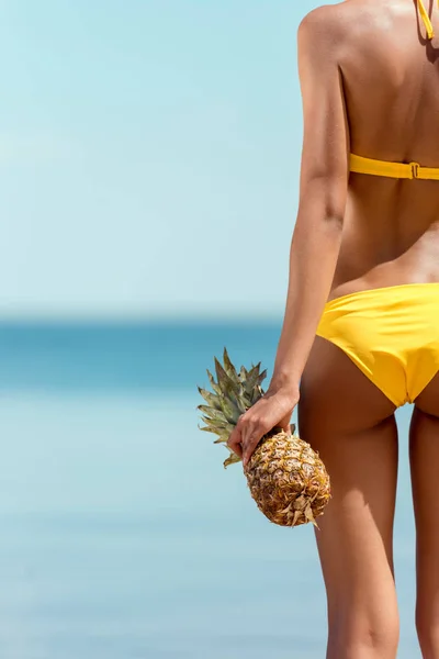 Cropped image of woman in bikini holding pineapple on sandy beach — Stock Photo