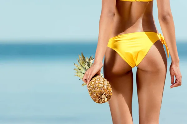 Abgeschnittenes Bild einer Frau im Bikini, die Ananas vor dem Meer hält — Stockfoto