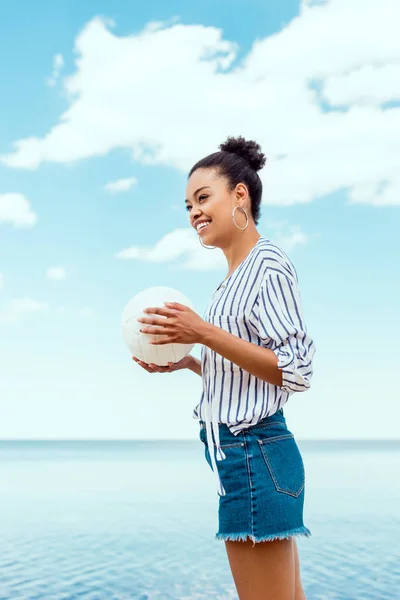 Blick auf lächelnde Afroamerikanerin mit Ball für Volleyball vor dem Meer — Stockfoto