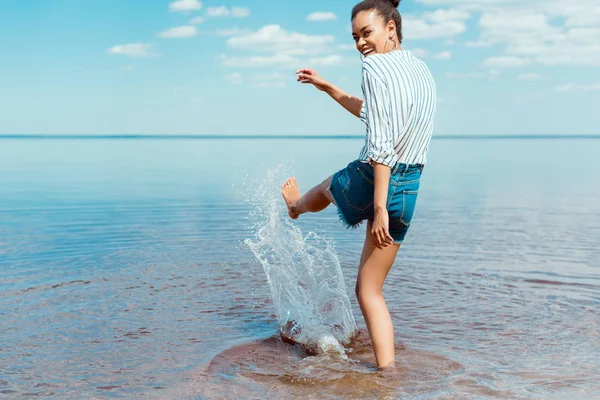 Happy african american woman kicking sea water — Stock Photo