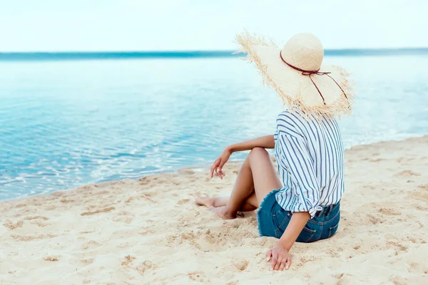 Visão traseira da jovem mulher em chapéu de palha relaxante na praia de areia — Fotografia de Stock