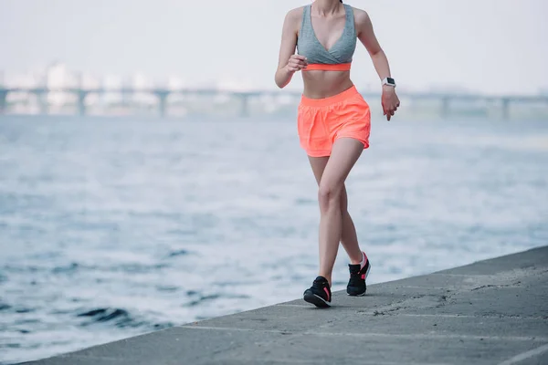 Cropped view of sportswoman jogging quay near river — Stock Photo