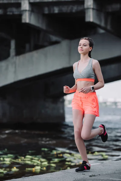 Beautiful sportswoman with smartwatch running on quay — Stock Photo