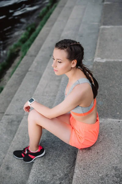 Chica deportiva con reloj inteligente sentado en las escaleras - foto de stock