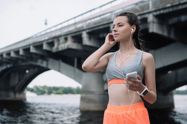 Young sportswoman with smartphone, earphones and smartwatch — Stock Photo