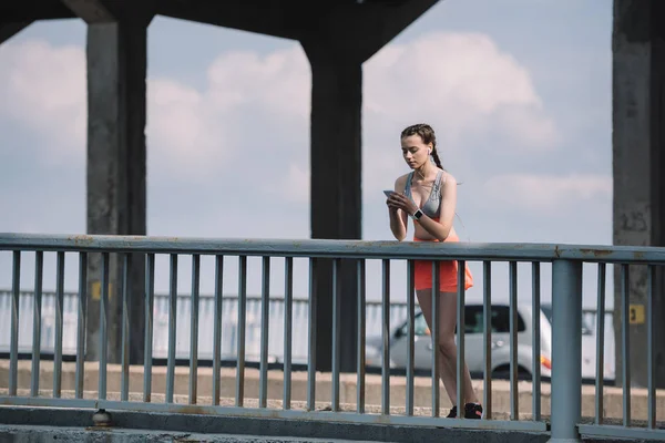 Sportswoman using smartwatch near railings on bridge — Stock Photo