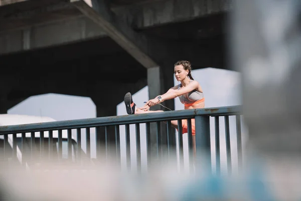 Atlética chica estiramiento pierna en barandillas en puente - foto de stock