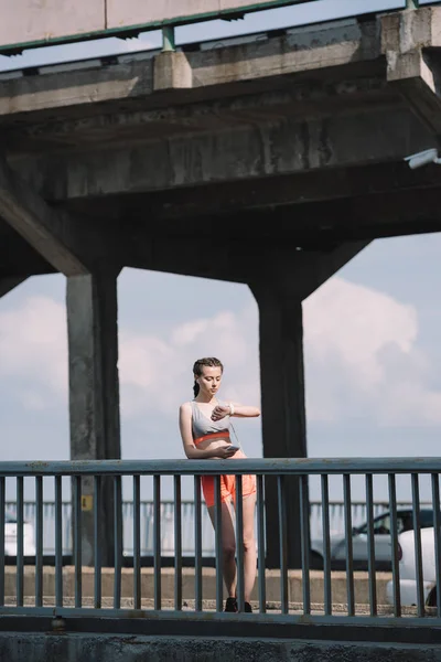 Schöne Sportlerin schaut auf Uhr und steht auf Brücke — Stockfoto