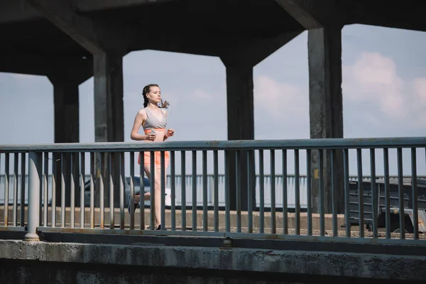 Hermosa deportista corriendo en el puente en la ciudad - foto de stock