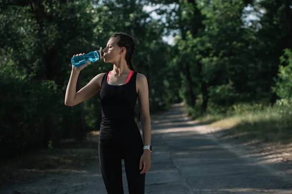 Attractive sportswoman drinking water in park — Stock Photo