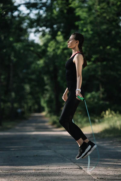 Beautiful athletic girl jumping on skipping rope on path in park — Stock Photo