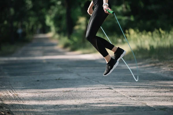 Cropped view of sportswoman jumping on skipping rope in park — Stock Photo