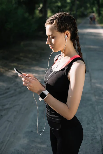 Deportista atractiva con auriculares, reloj inteligente y teléfono inteligente - foto de stock