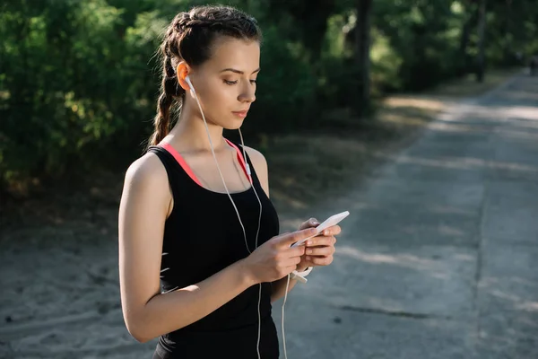 Sportliche Frau hört Musik mit Kopfhörern und nutzt Smartphone — Stockfoto