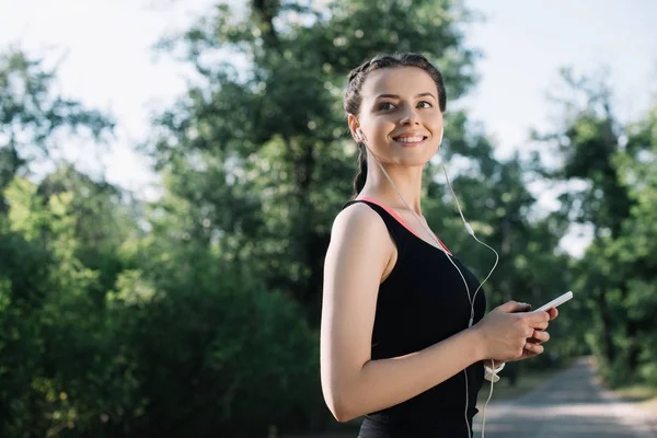 Bellissima sportiva sorridente che ascolta musica con auricolari e smartphone — Foto stock