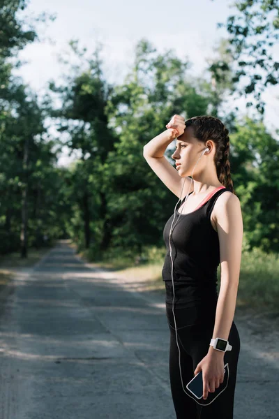 Écouteurs femme athlétique fatigué, montre intelligente et smartphone — Photo de stock