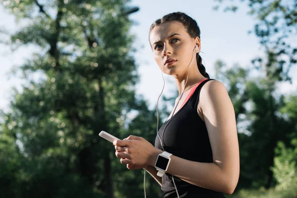 Schöne Sportlerin mit Smartwatch, die mit Kopfhörern und Smartphone Musik hört — Stockfoto