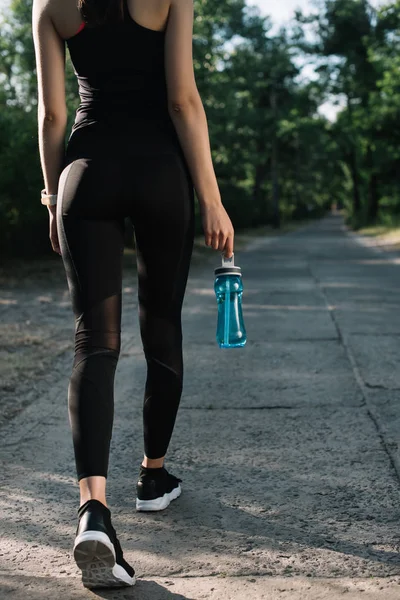 Back cropped view of sportswoman with bottle of water walking on path — Stock Photo