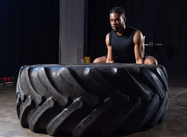 Athletic african american man exercising with tyre and looking away in gym — Stock Photo