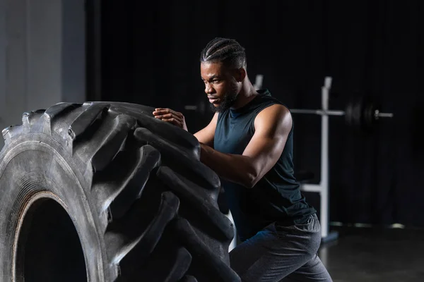 Зосереджений молодий афроамериканський спортсмен тренування з шиною в тренажерному залі — стокове фото