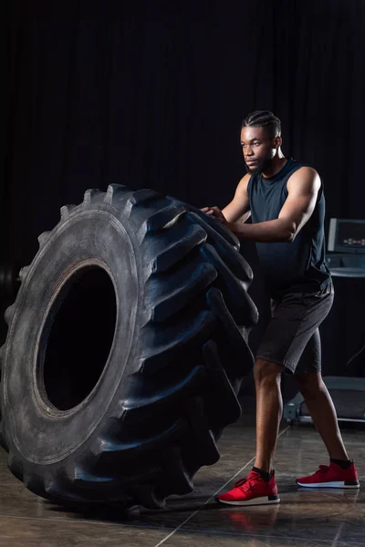 Vue pleine longueur de l'entraînement de l'homme afro-américain athlétique avec pneu et détourner les yeux — Photo de stock