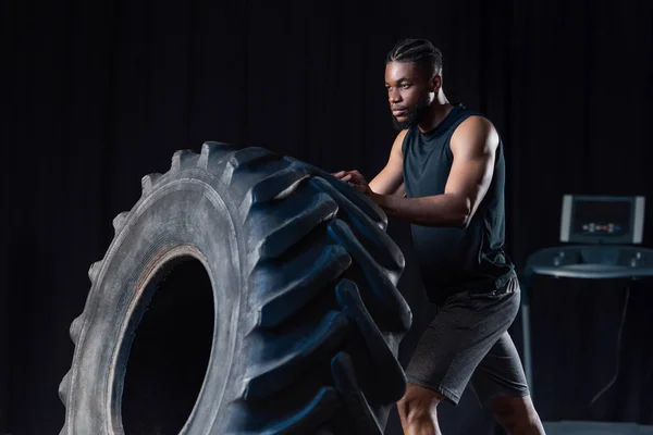 Entraînement sportif afro-américain sérieux avec pneu et détournement des yeux — Photo de stock