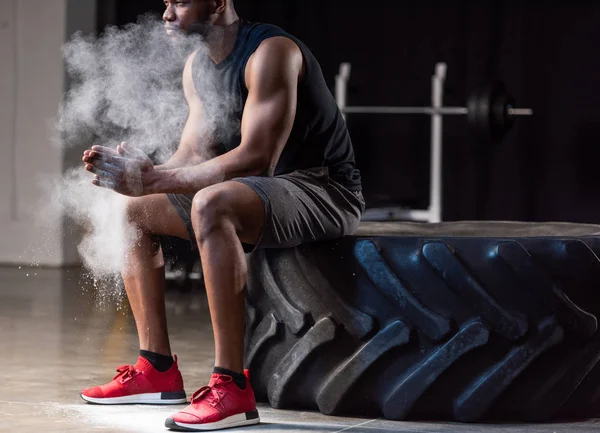 Cropped shot of african american sportsman sitting in tyre and applying talcum powder on hands — Stock Photo