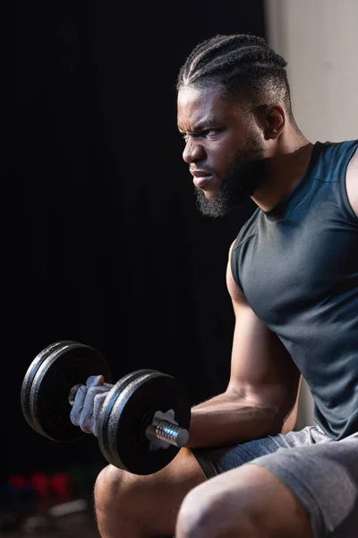 Serious african american sportsman exercising with dumbbell and looking away — Stock Photo