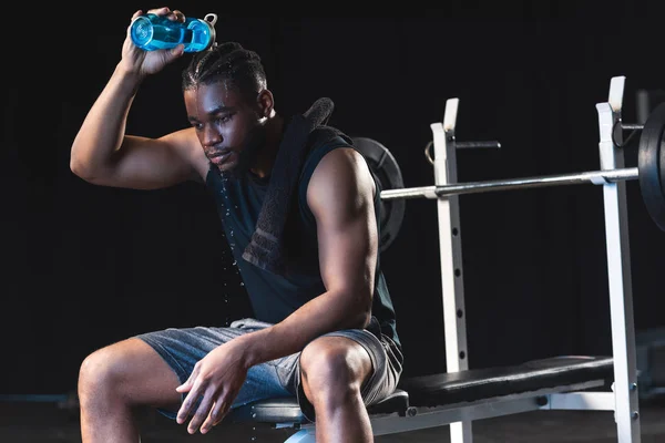 Sudoroso afroamericano deportista verter agua en la cabeza después del entrenamiento en el gimnasio - foto de stock
