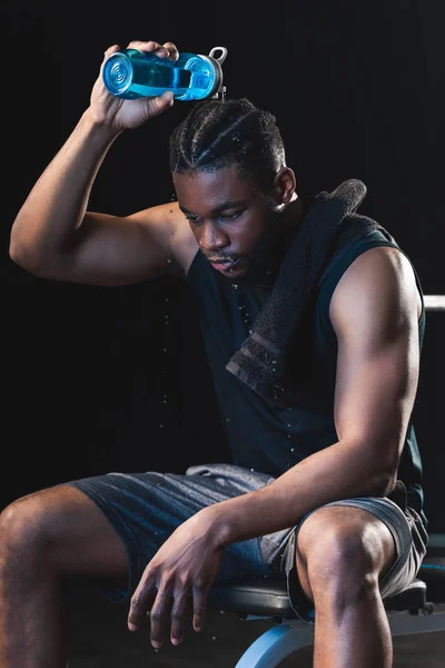 Tired african american sportsman pouring water on head while sitting after workout in gym — Stock Photo