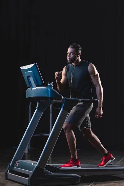 Full length view of young african american man in earphones exercising on treadmill and looking away — Stock Photo
