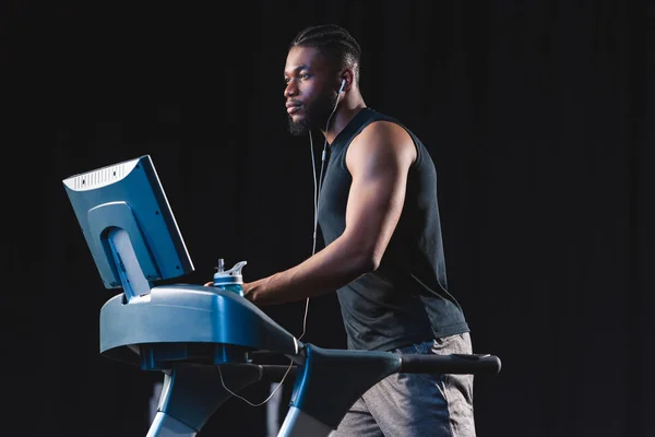 Guapo joven afroamericano hombre en auriculares haciendo ejercicio en la cinta de correr y mirando hacia otro lado - foto de stock