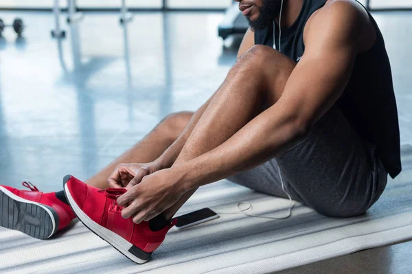 Plan recadré de jeune sportif afro-américain attachant des lacets dans la salle de gym — Photo de stock