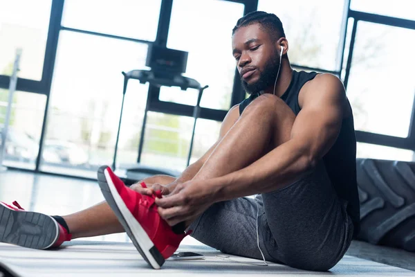 Vue à angle bas de jeune sportif afro-américain attachant des lacets dans la salle de gym — Photo de stock
