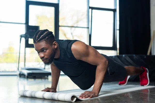 Muscular afroamericano deportista haciendo flexiones y mirando hacia otro lado en el gimnasio - foto de stock