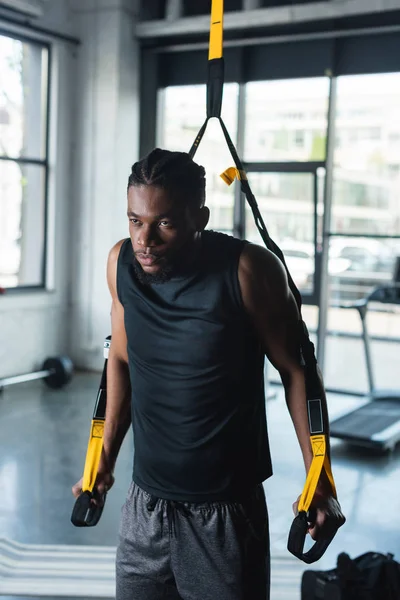 Serio joven afroamericano deportista entrenamiento con correas de fitness en el gimnasio - foto de stock