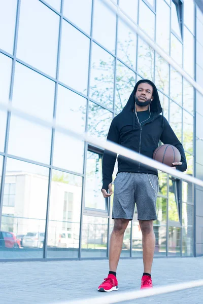 Vue en angle bas du beau sportif afro-américain tenant le ballon de basket dans la rue — Photo de stock