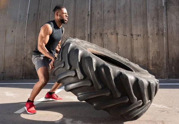 Side view of concentrated african american sportsman training with tire on street — Stock Photo