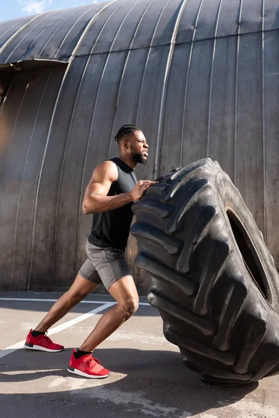 Athletic african american man exercising with tire on street — Stock Photo