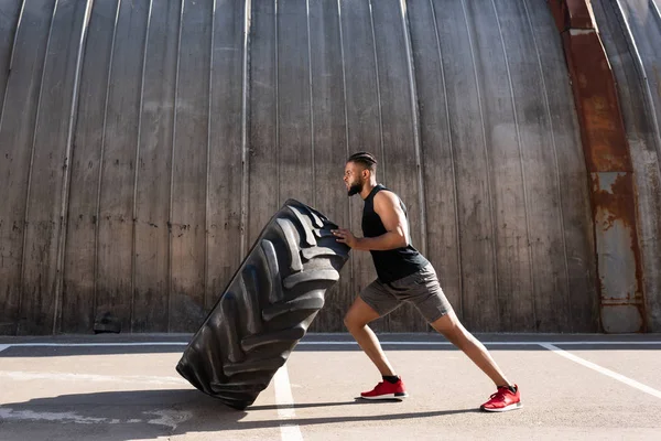 Seitenansicht des muskulösen afrikanisch-amerikanischen Sportlers, der mit Reifen auf der Straße trainiert — Stockfoto