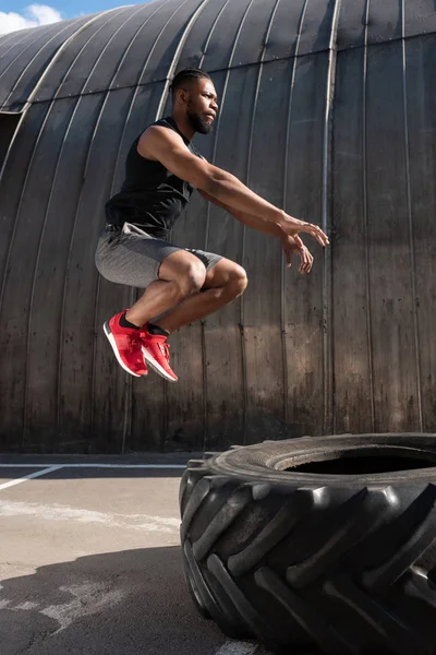 Side view of muscular african american man jumping while training with tyre on street — Stock Photo