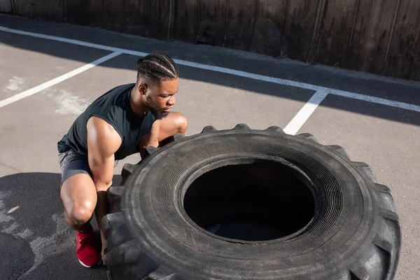 Високий кут зору м'язистий афроамериканський спортсмен вправляється з шиною на вулиці — стокове фото
