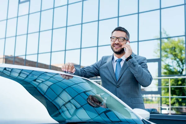 Portrait d'un homme d'affaires souriant parlant sur smartphone alors qu'il se tenait debout en voiture dans la rue — Photo de stock