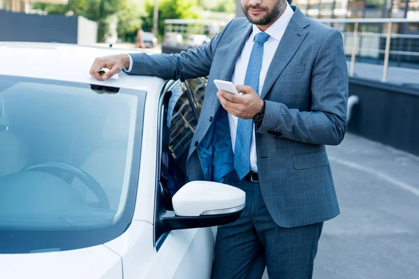 Partial view of businessman using smartphone while standing at car on street — Stock Photo