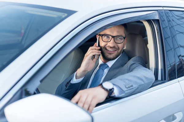 Retrato de un hombre de negocios sonriente hablando en el teléfono inteligente mientras conduce el coche - foto de stock