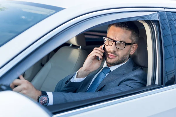 Retrato de homem de negócios em óculos falando no smartphone enquanto dirige carro — Fotografia de Stock